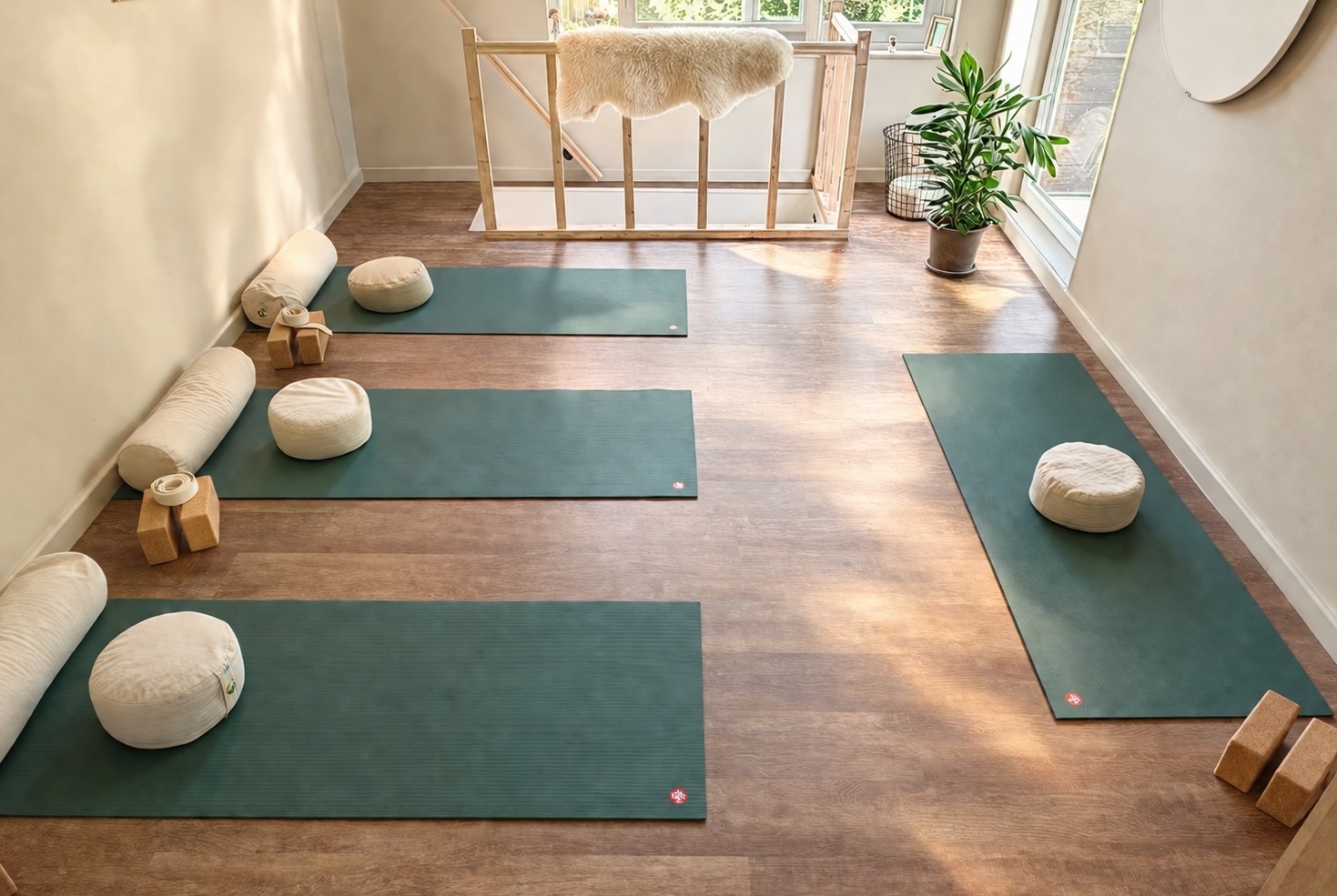 De studio van bovenaf: yogamatten met bolsters, kussens en blokken klaargelegd op een houten vloer
